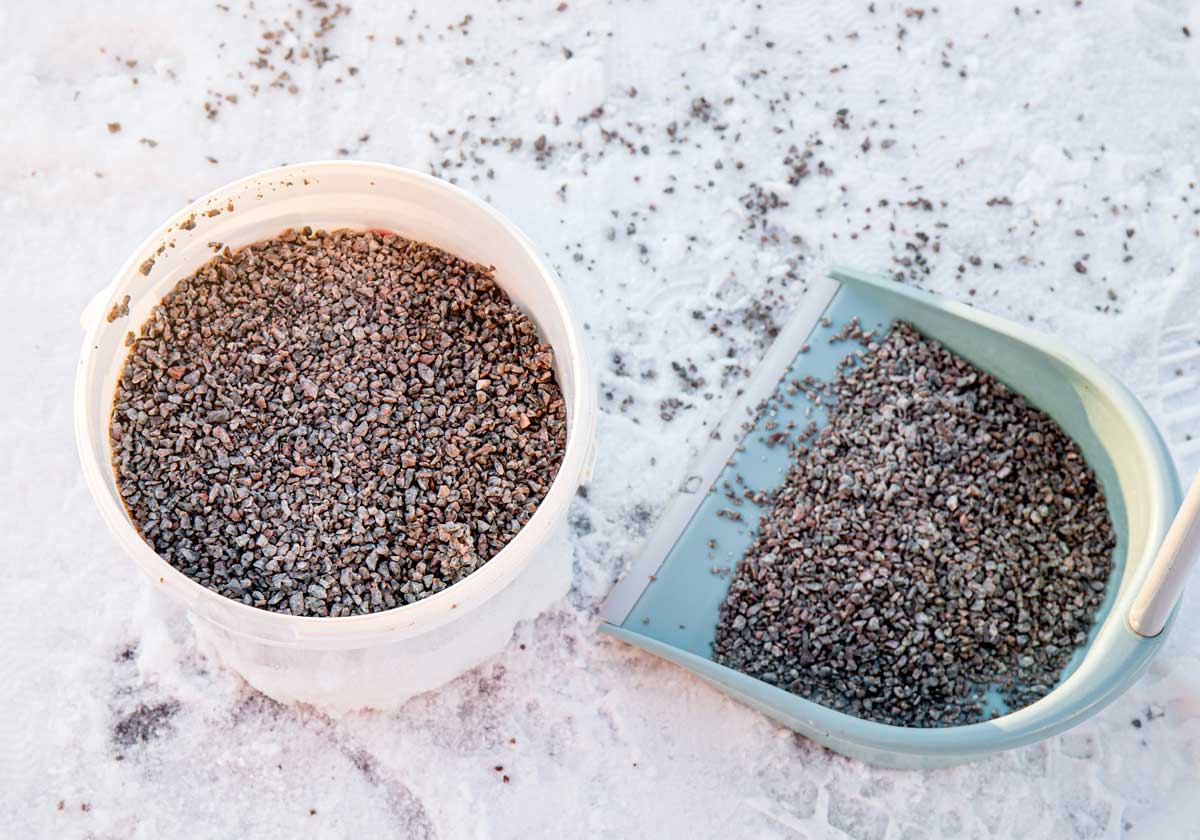 Posypový štěrk v plastové nádobě a lopatce připravený k použití na zledovatělý povrch