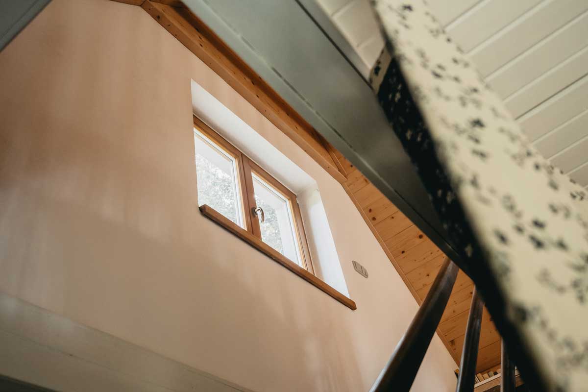 Světlo pronikající oknem zvýrazňuje strukturu dřeva a klidnou atmosféru domu.