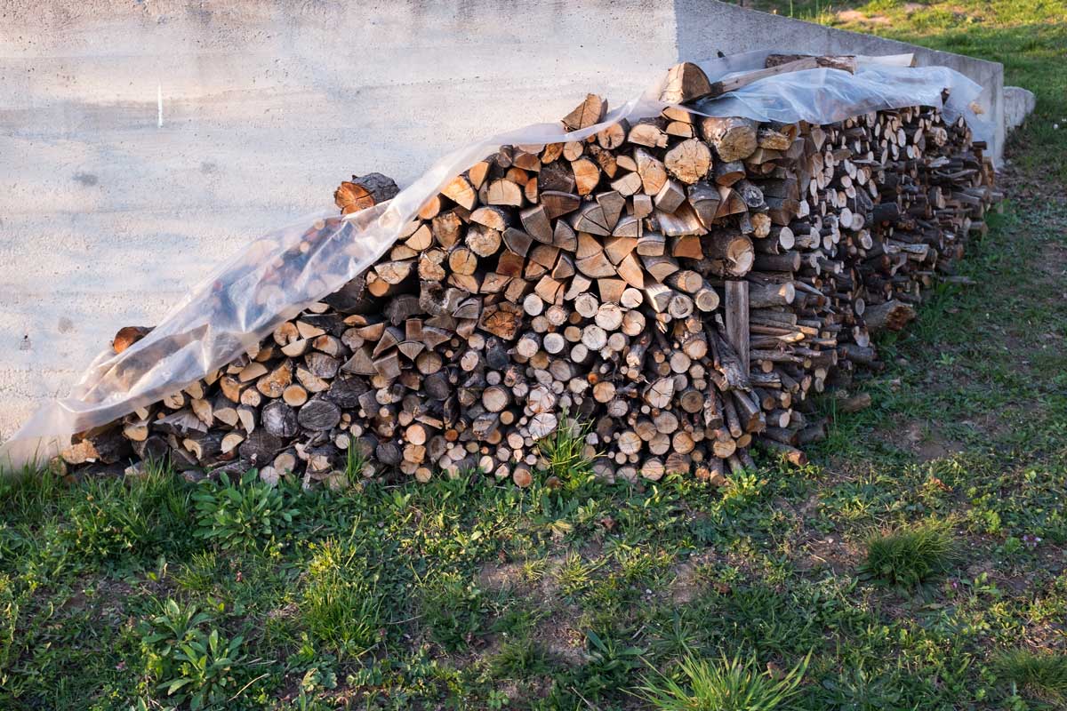 Palivové dřevo uložené pod fólií opřené o zeď domu, chráněné před deštěm.