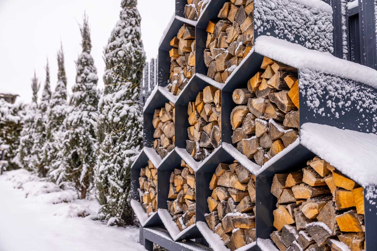 Moderní kovový regál s palivovým dřevem pokrytým zimním sněhem.