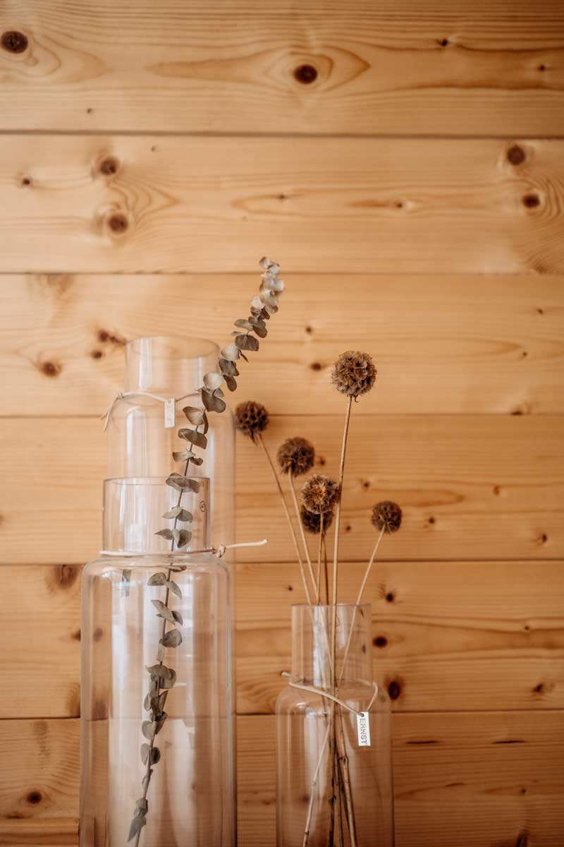 Sušené květy a sklo tvoří jednoduchou, ale výraznou dekoraci inspirovanou lesem.