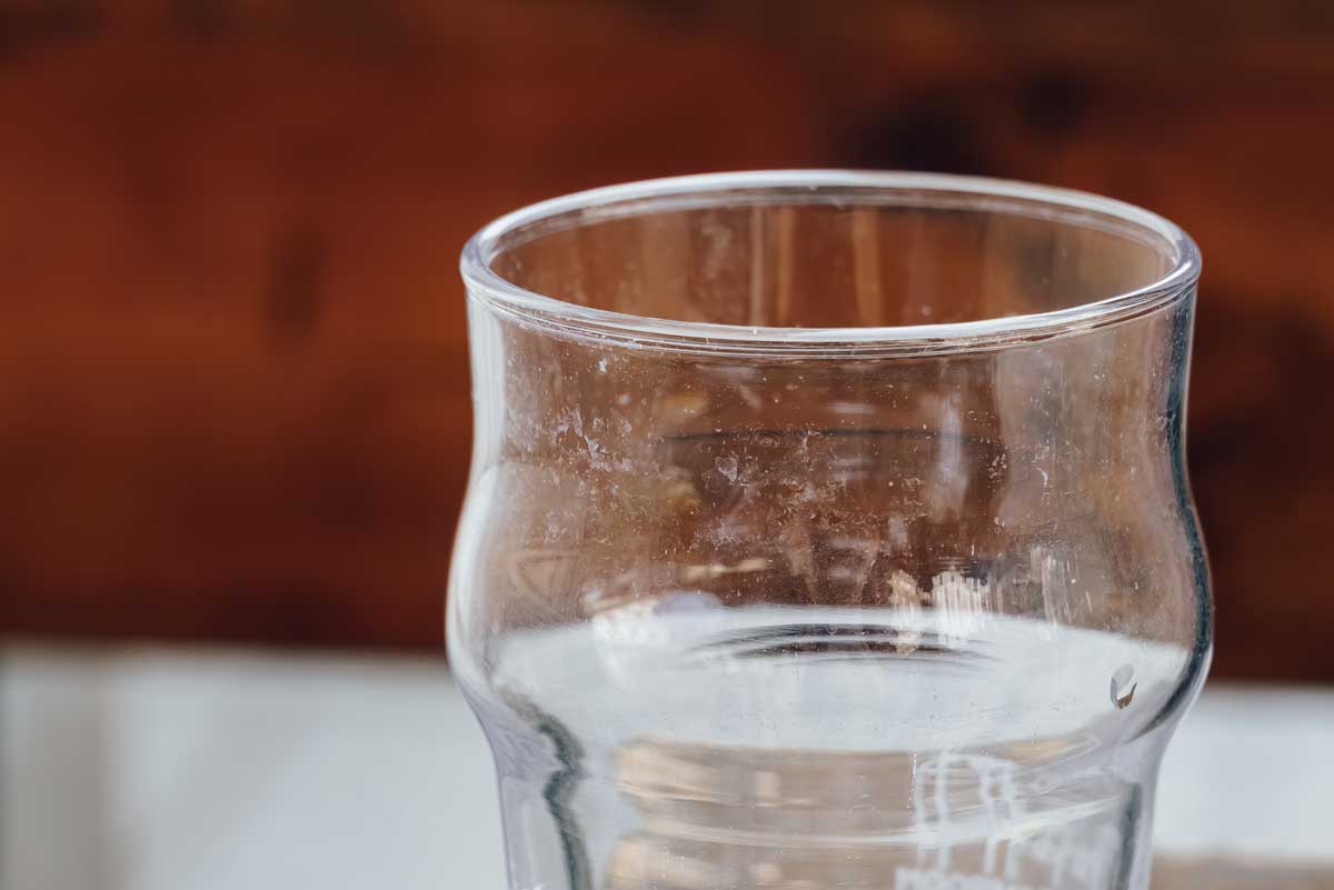 Detail zamlžené sklenice s viditelnými skvrnami po tvrdé vodě.