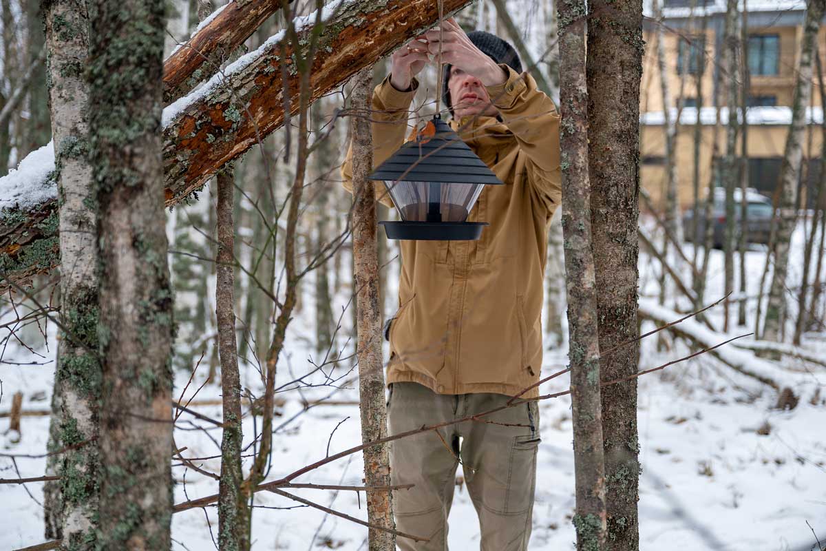 zavesne krmitko Muž v zimním oblečení zavěšuje krmítko pro ptáky mezi stromy pokrytými sněhem.