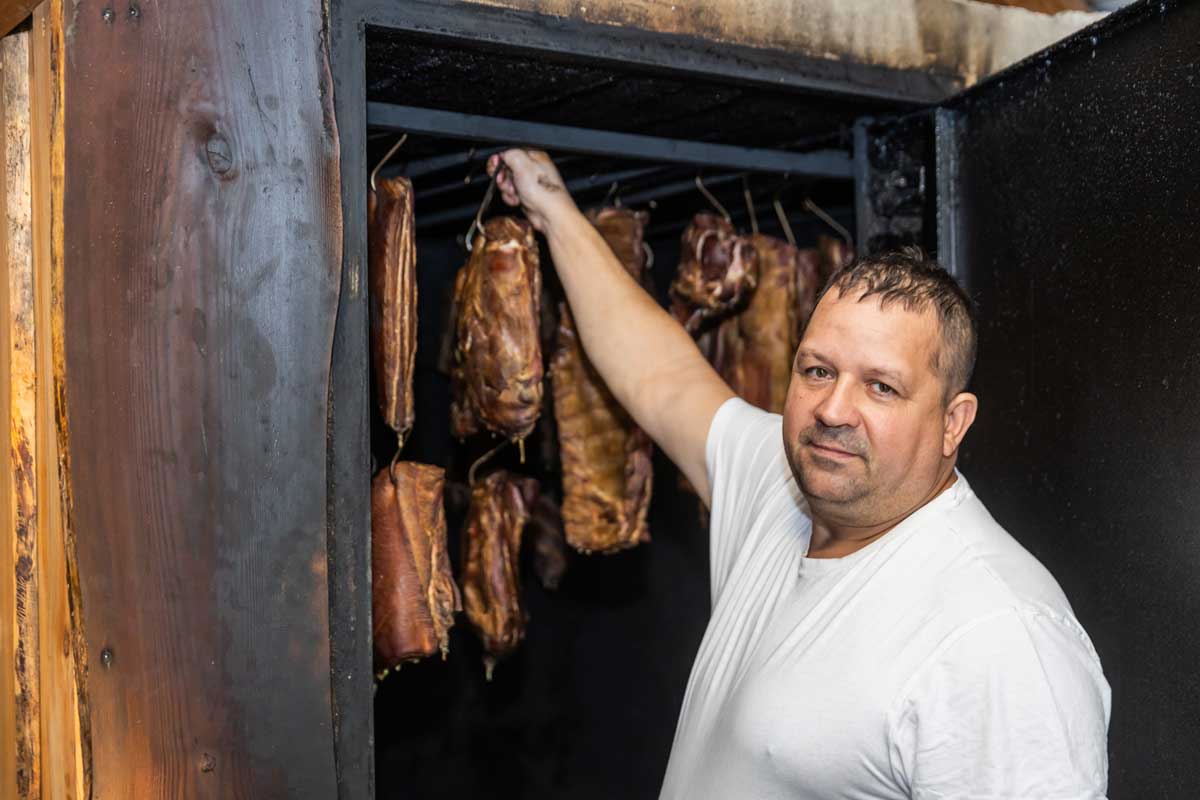 Řezník kontroluje zavěšené kusy masa v udírně při výrobě domácích klobás