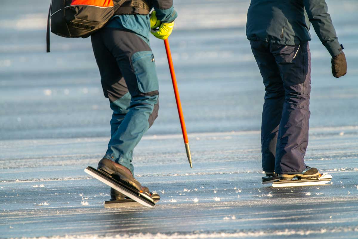 Bruslaři na zamrzlém jezeře kontrolují led pomocí hole, aby snížili riziko vstupu na slabá místa.