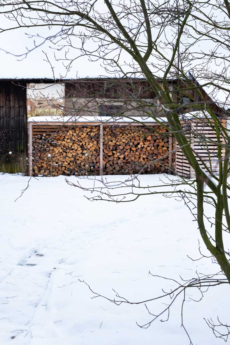 Dřevník u stodoly zaplněný nařezaným dřevem, který je praktickou součástí zahrady i v zimě.
