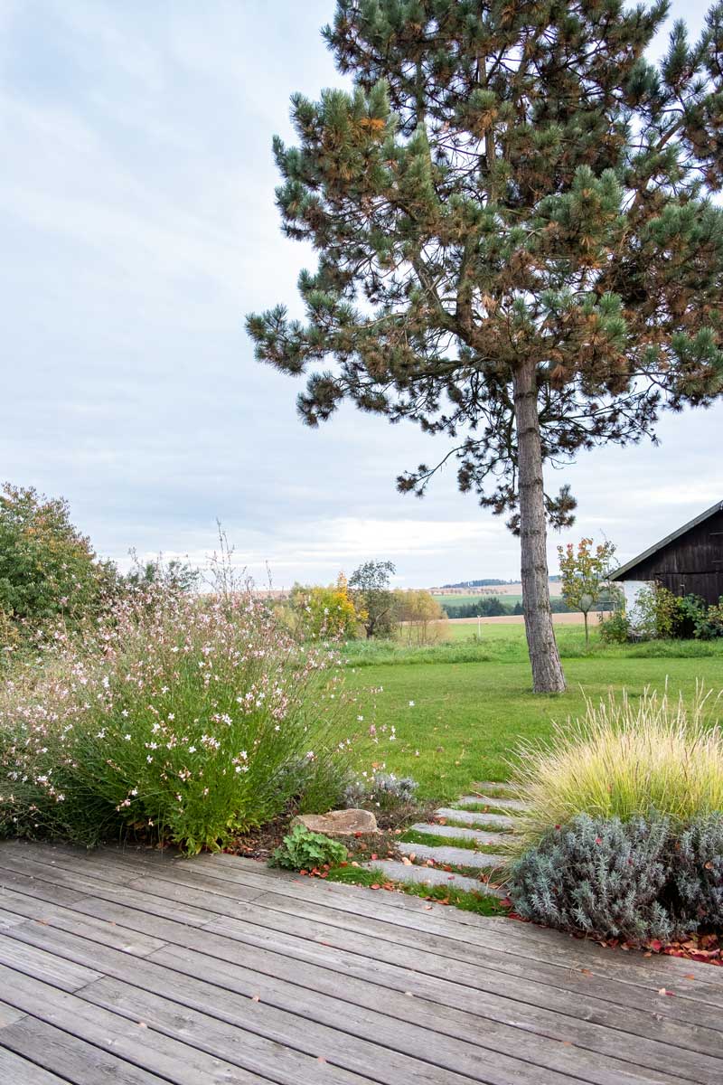 Z dřevěné terasy u domu se nabízí malebný výhled do zahrady i okolní krajiny. Její okraje lemuje trvalková výsadba.