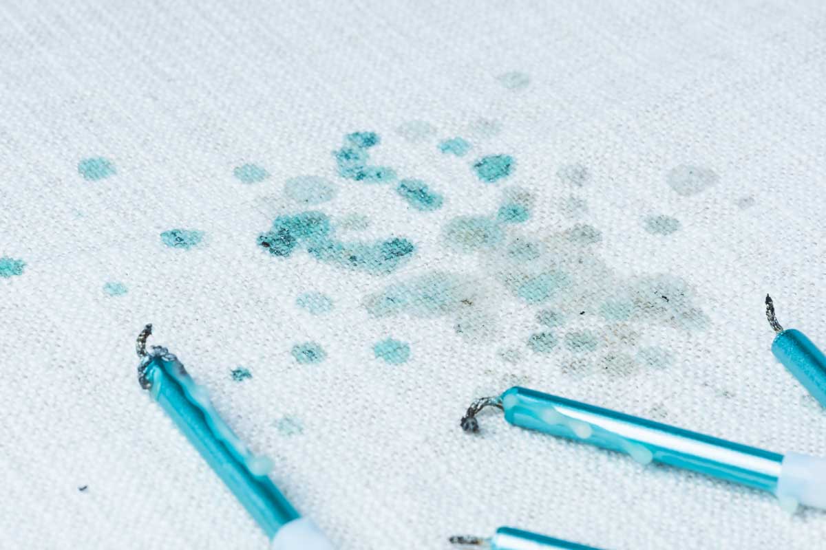 Skvrny od modrého vosku na bílé textilii po rozteklé svíčce