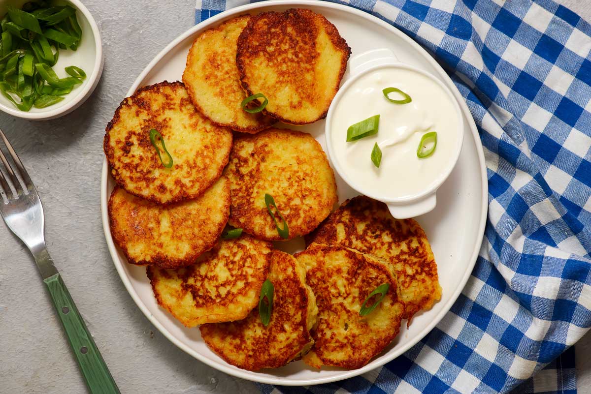 Křupavé lotyšské bramborové placky kartupeļu pankūkas podávané se zakysanou smetanou a posypané jarní cibulkou.