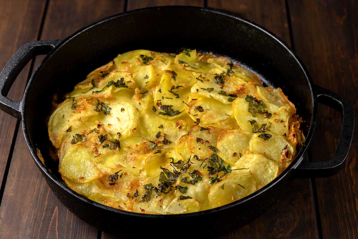 Vrstvené plátky brambor Pommes Anna zapečené na másle a podávané jako zlatavý kompaktní koláč.