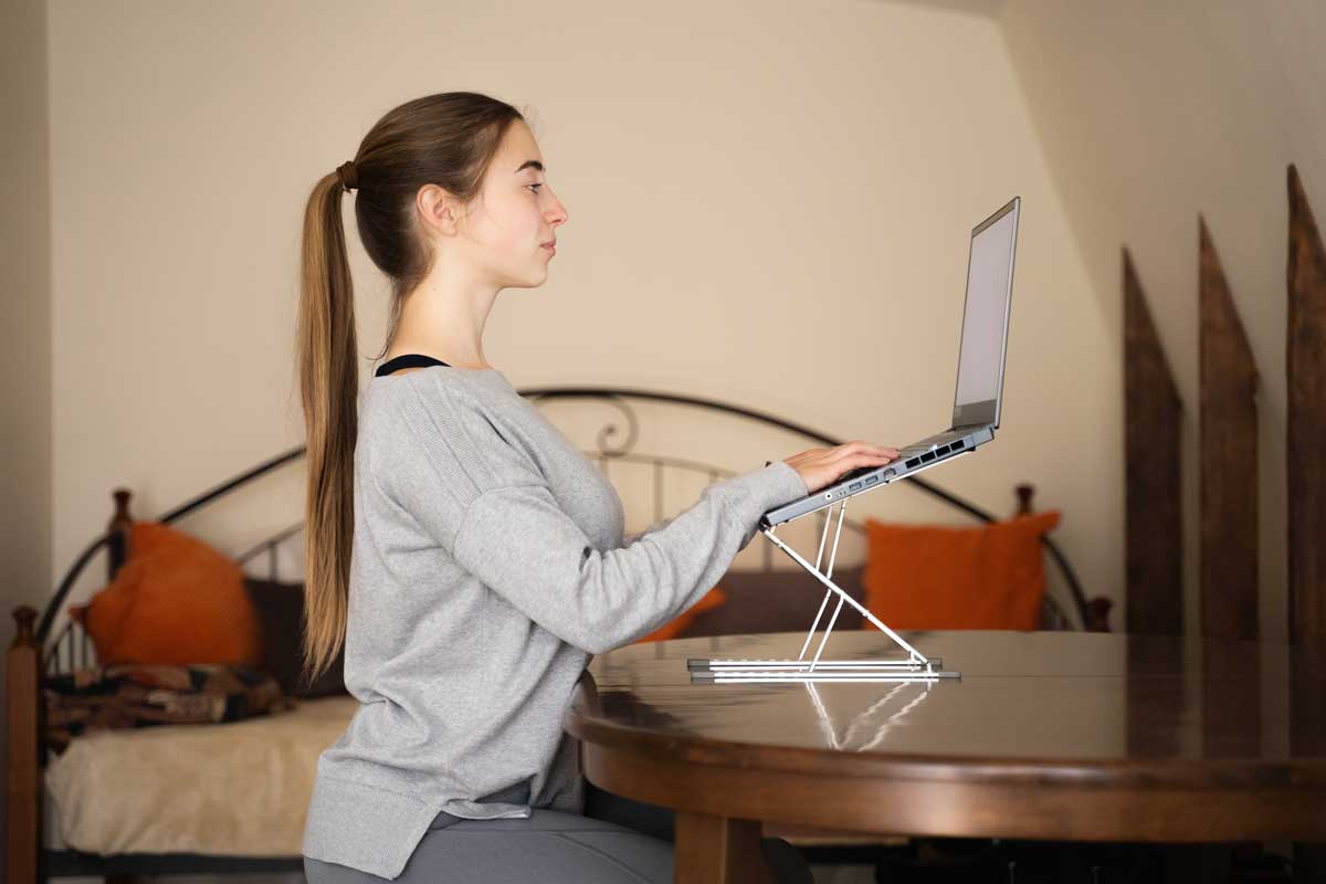 spravna pozice monitoru Žena pracuje na notebooku umístěném na stojanu v úrovni očí – správná výška monitoru pomáhá snižovat únavu očí a krční páteře.