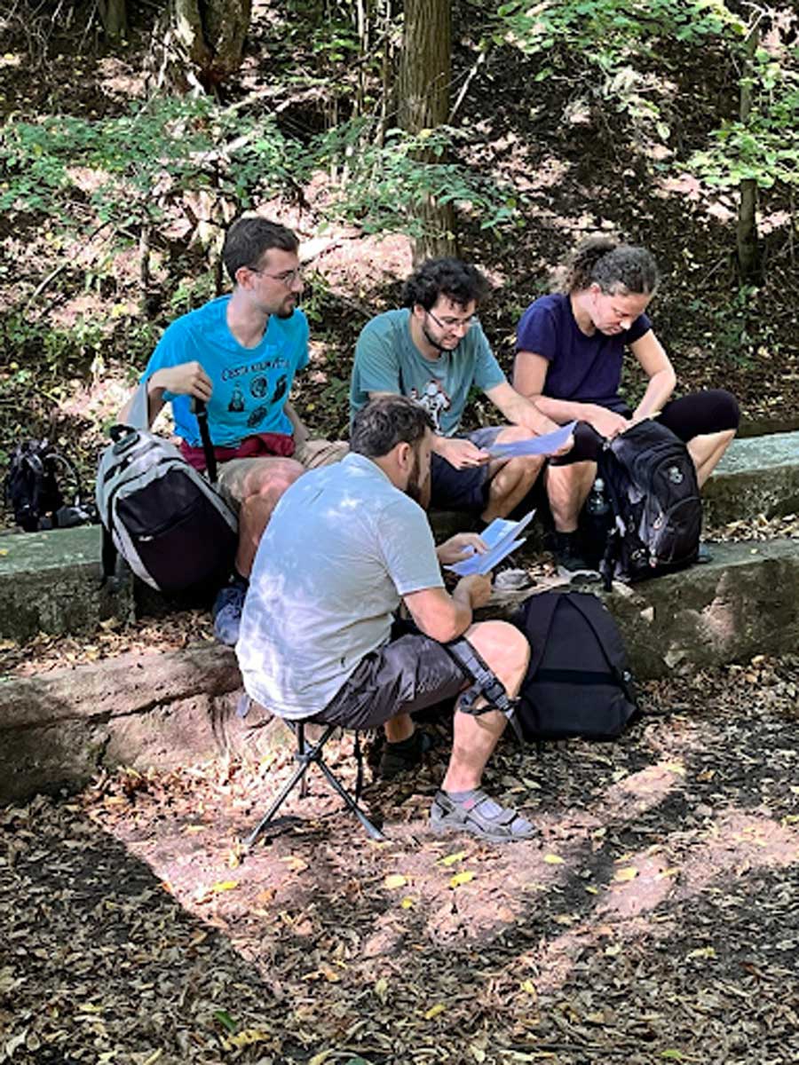 Tým hráčů sedí v lese a společně luští zadání šifry během hry.