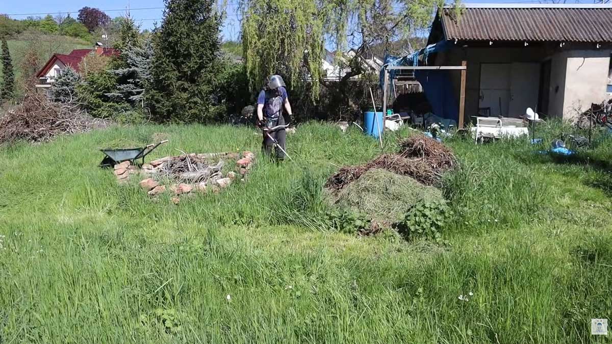 Přerostlá tráva a neudržované kouty kolem kůlny ukazují původní stav zahrady před zahájením prací.