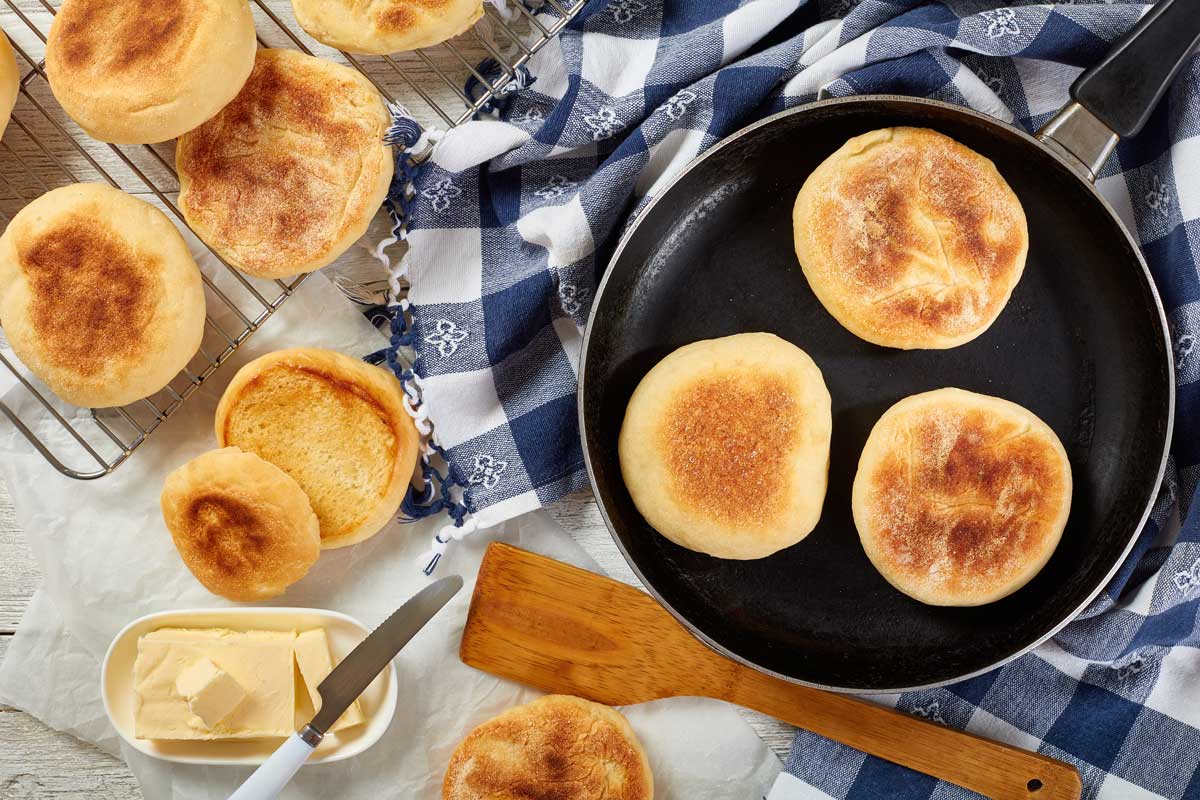 English muffins opečené na pánvi a odložené na mřížce vedle másla a utěrky.