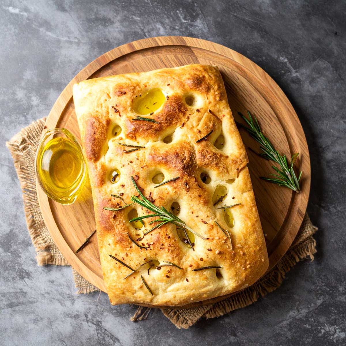 Italská focaccia s olivami rozmarýnem a olivovým olejem upečená dozlatova na dřevěném prkénku.