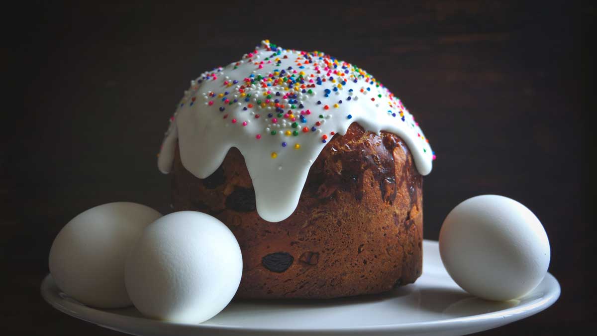 Ukrajinská paska s bílou polevou a barevným zdobením podávaná s vejci na talíři.