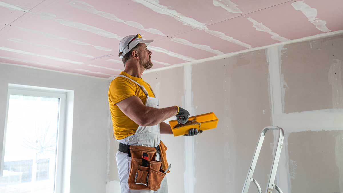 Řemeslník tmelením dokončuje spoje sádrokartonového stropu po montáži desek a připravuje povrch na další úpravy
