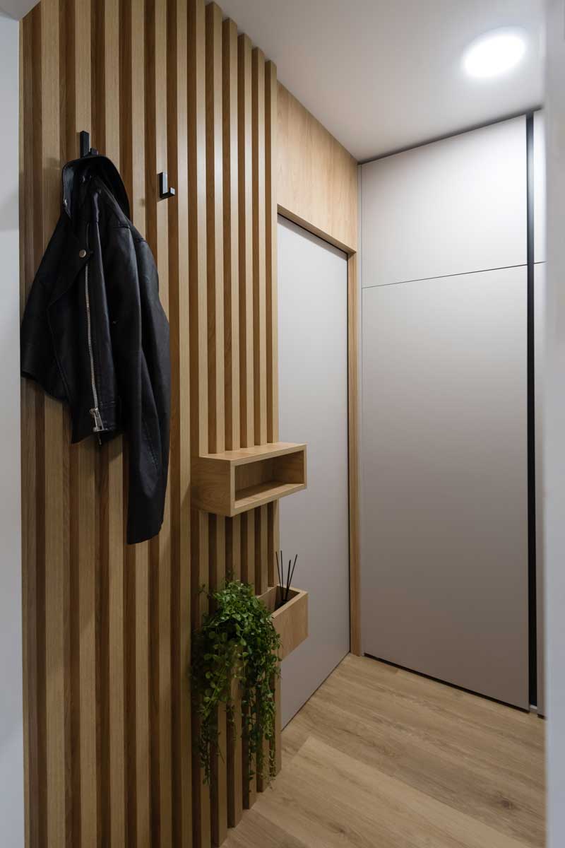 Moderní chodba s dřevěnými lamelami háčky na kabáty a vestavěnou skříní po celé výšce stěny.