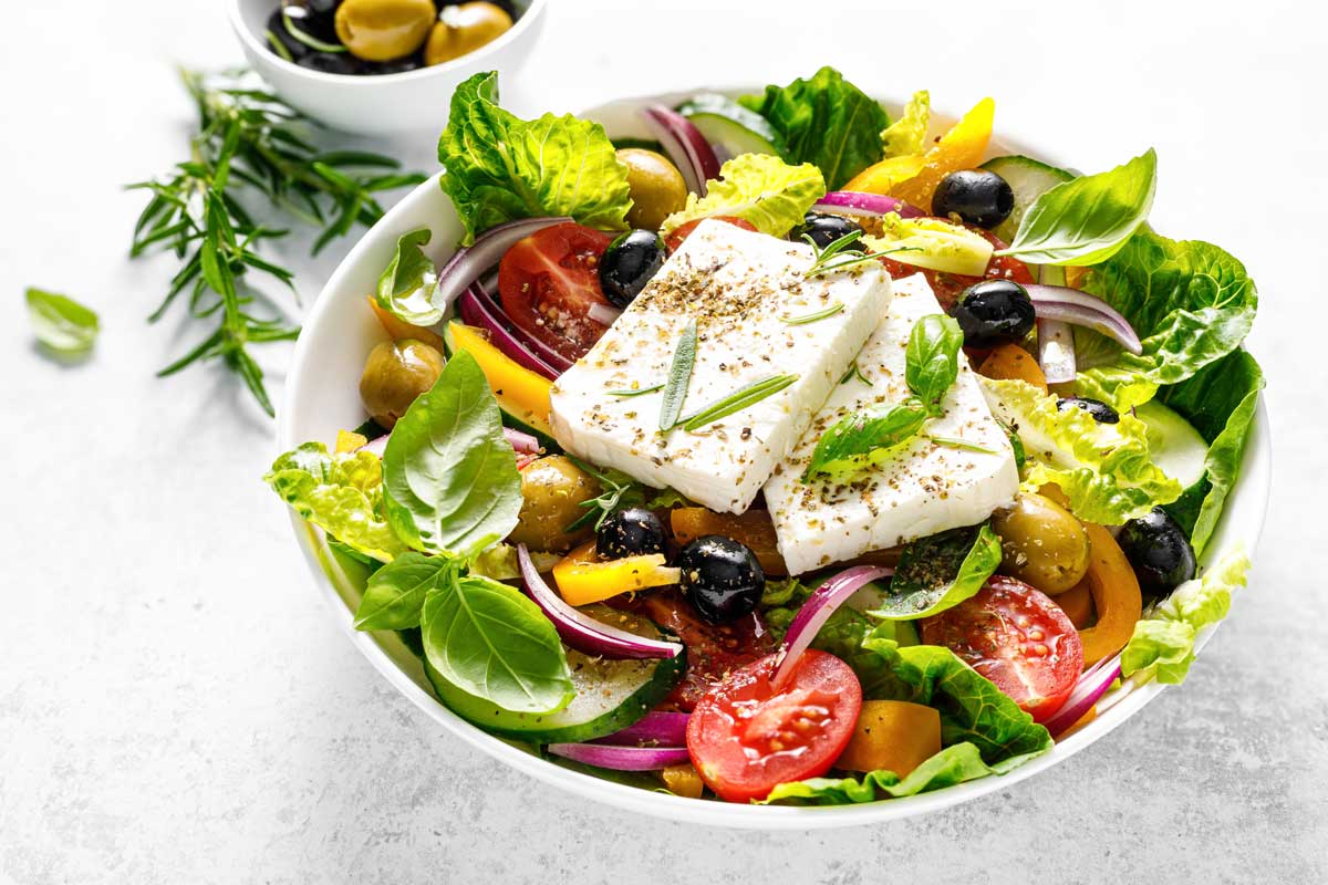 Řecký salát s feta sýrem, olivami a čerstvou zeleninou doplněný bylinkami.