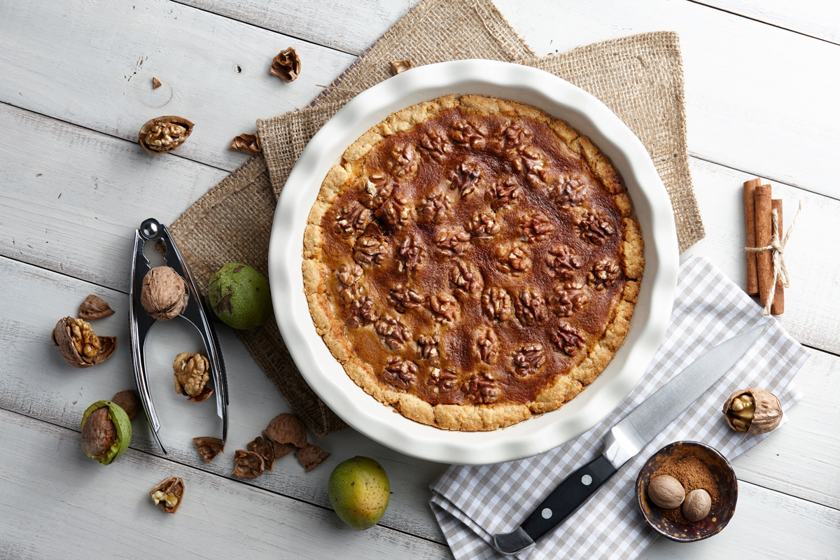 Koláč s vlašskými ořechy a karamelovou náplní na dřevěném stole láká svou křupavou strukturou a bohatou chutí.