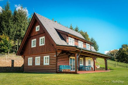 Exteriér roubenky se sedlovou střechou zasazené do horské přírody.