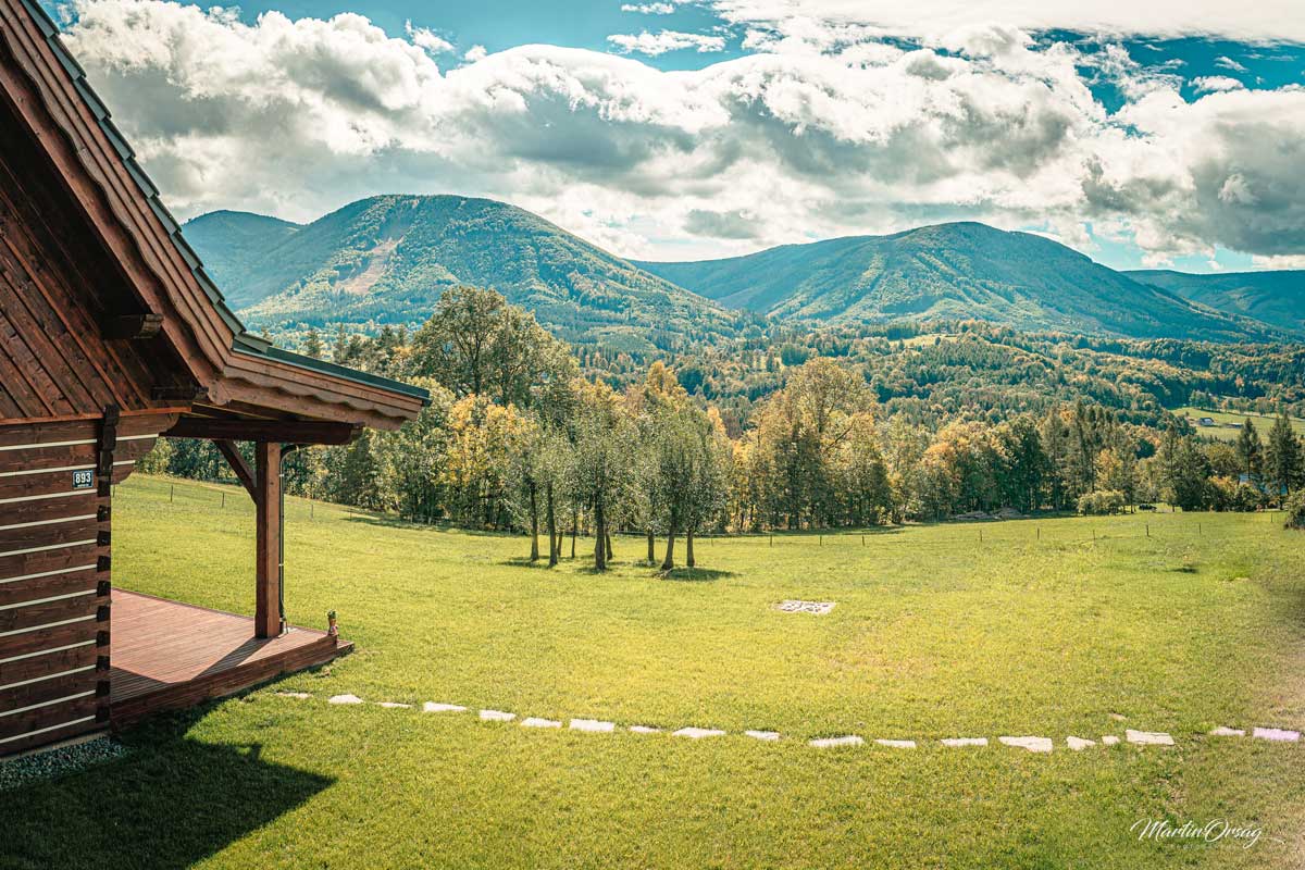 Výhled z roubenky na horskou krajinu s terasou a přírodní zahradou.
