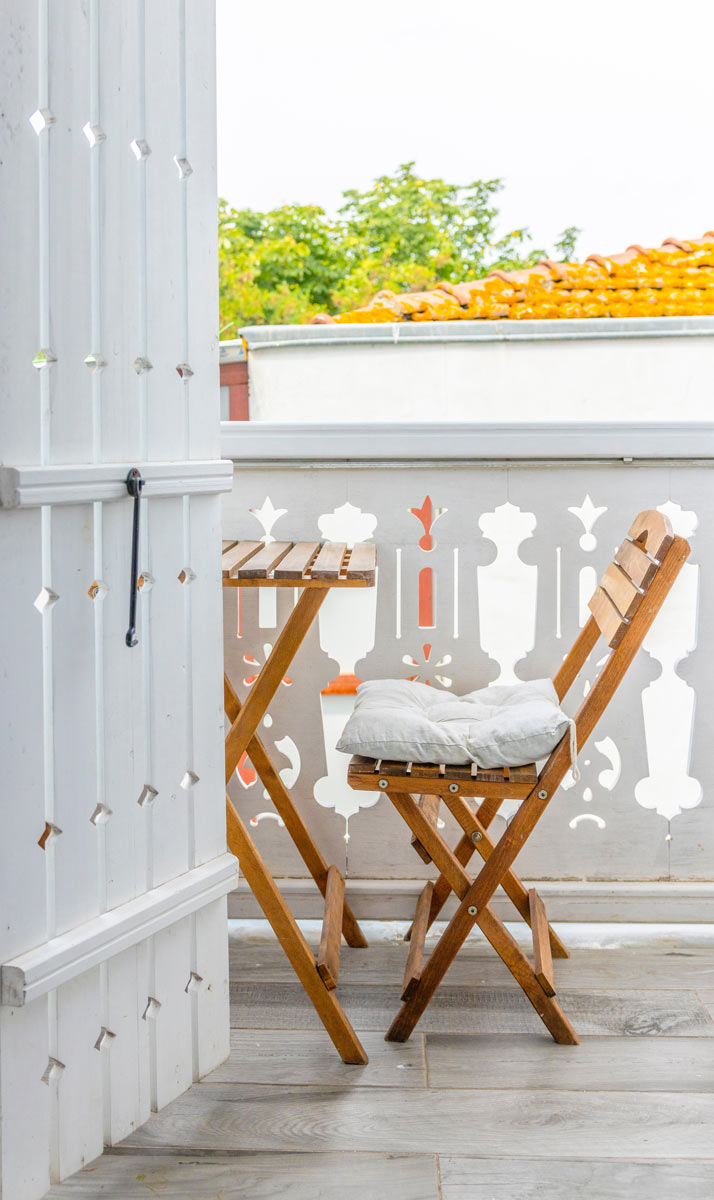 Balkon s dřevěnou skládací židlí, stolkem a světlým podsedákem připravený k posezení.