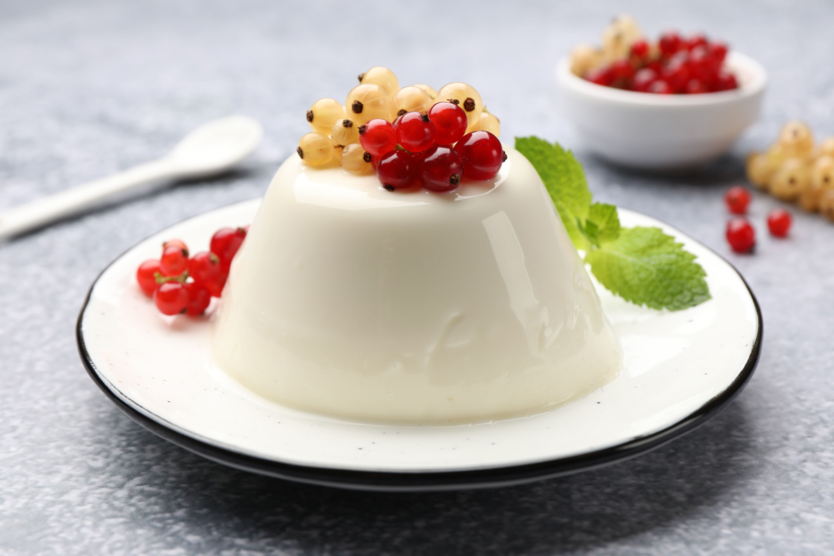 Jemná panna cotta ozdobená rybízem představuje elegantní dezert s květinovou vůní bezu.