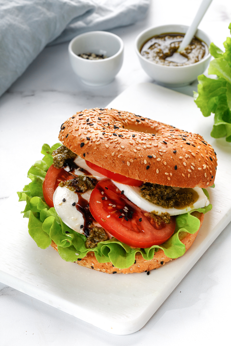 Sezamový bagel je naplněný mozzarellou, rajčaty, listovým salátem a bazalkovým pestem.