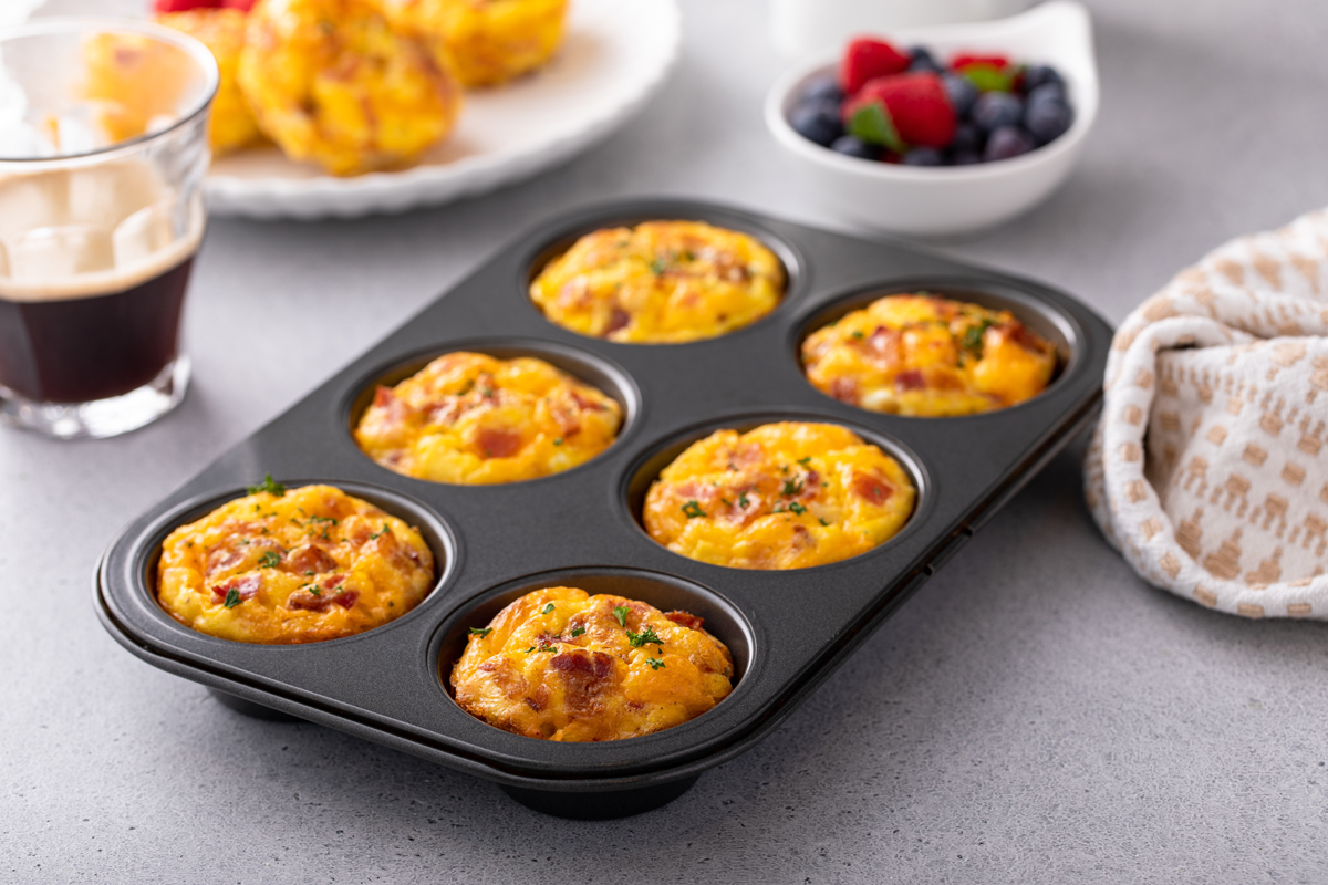 Ve formě na muffiny jsou upečené nadýchané vaječné muffiny s kousky zeleniny a sýra.