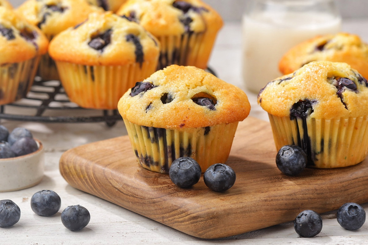 Nadýchané borůvkové muffiny s čerstvými borůvkami na dřevěném prkénku.