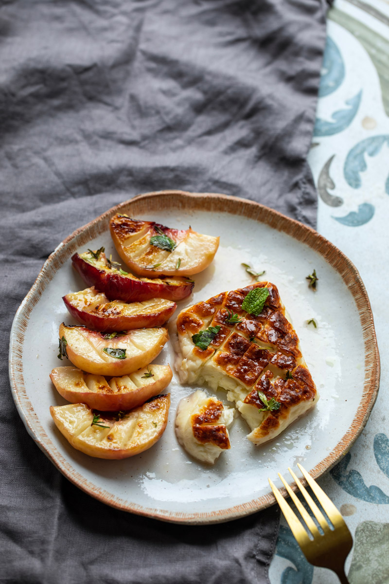 Grilovaný sýr halloumi je podávaný s opečenými broskvemi, bylinkami a medovou zálivkou.