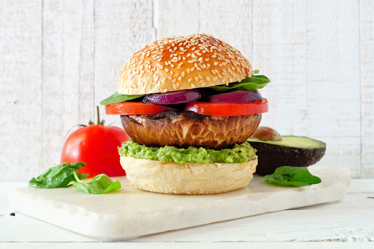 Burger z velké houby portobello je doplněný avokádovou pomazánkou, rajčetem a červenou cibulí.