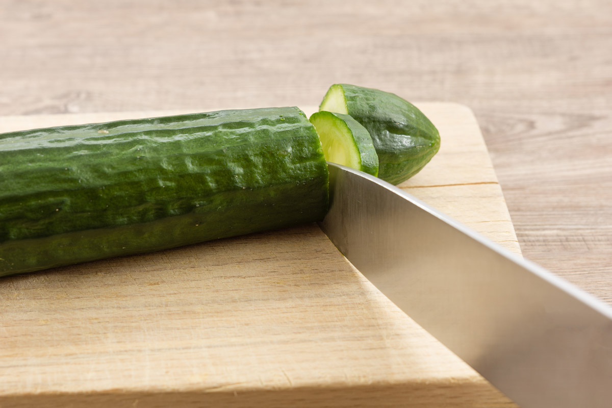 konce okurky Odkrojení koncové části čerstvé okurky nožem na kuchyňském prkénku.