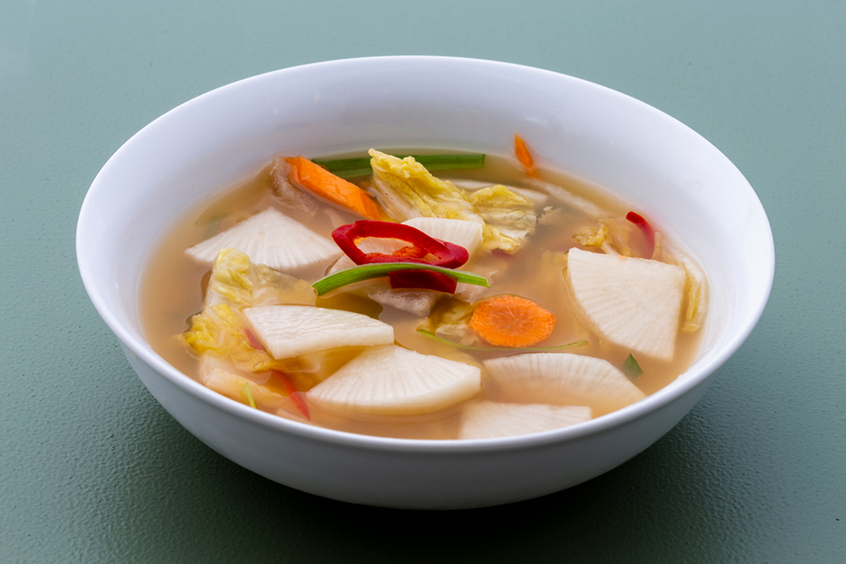 Nabak kimchi z plátků ředkve a pekingského zelí ve světlém fermentovaném nálevu.