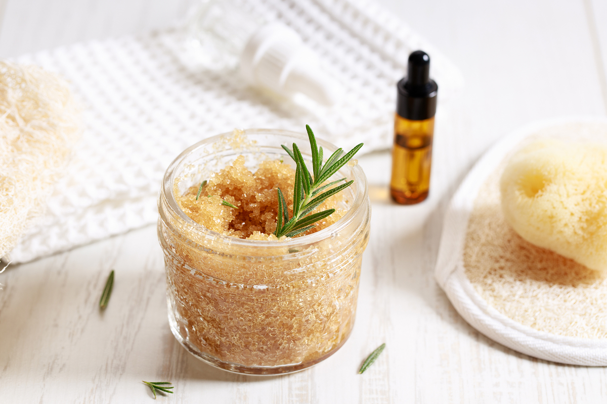 telovy peeling 1 Domácí cukrový tělový peeling s větvičkou čerstvého rozmarýnu ve skleněné nádobě.