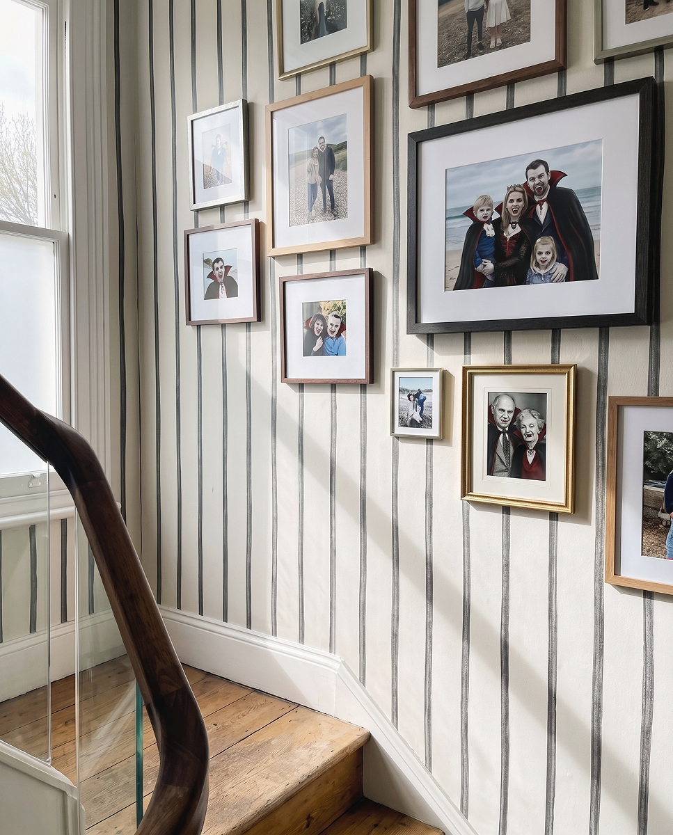 feathr.com 1 Galerie rodinných fotografií na stěně schodiště, na kterých mají někteří členové rodiny podobu upírů s výraznými zuby a tmavými plášti.