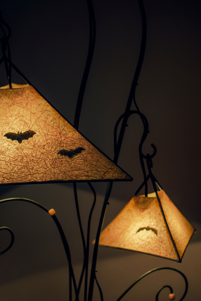 lampa dekorace 1 Dvě rozsvícené lampy s papírovými stínidly zdobenými černými siluetami netopýrů vytvářejí halloweenskou atmosféru.