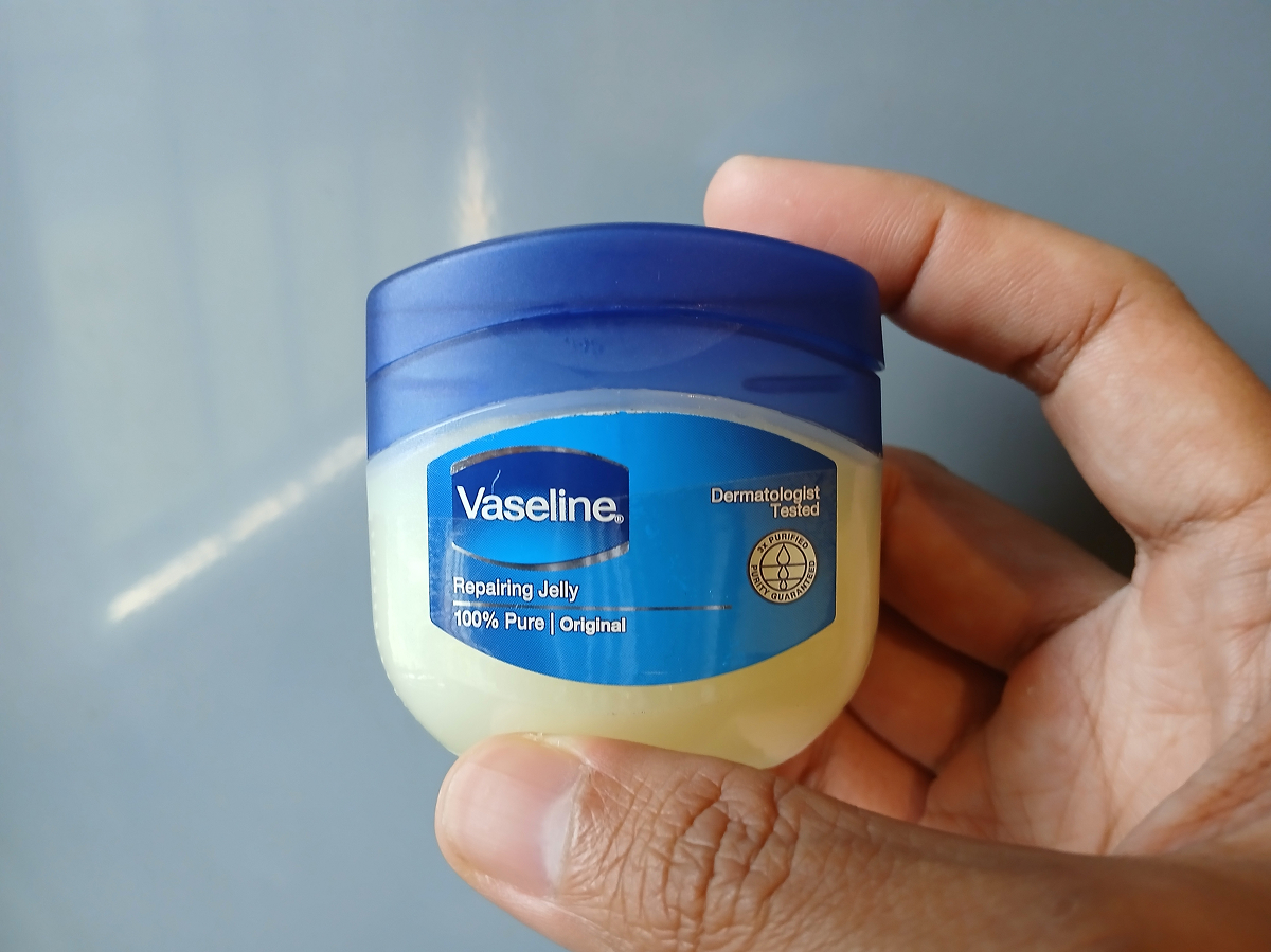 vazelina 1 Malá plastová nádobka kosmetické vazelíny s modrým víčkem a etiketou Vaseline, kterou člověk drží v ruce.